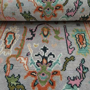 May include: A rolled-up gray rug with a detailed floral pattern. The design incorporates orange, green, pink, and teal elements. The rug's border features a complementary color scheme, enhancing the overall aesthetic. The rug is made of a soft, textured material.