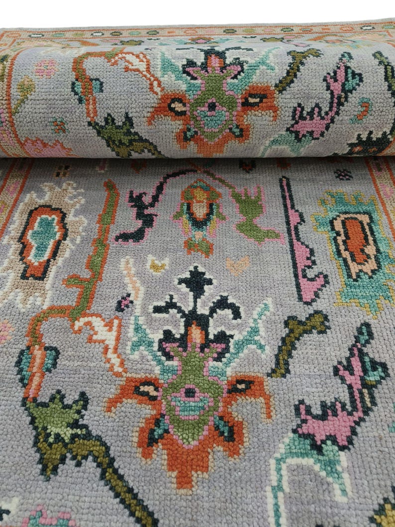 May include: A rolled-up gray rug with a detailed floral pattern. The design incorporates orange, green, pink, and teal elements. The rug's border features a complementary color scheme, enhancing the overall aesthetic. The rug is made of a soft, textured material.