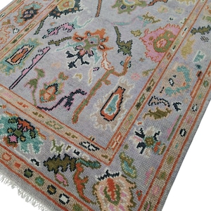 May include: A rectangular area rug with a light gray background and a colorful floral pattern. The rug features a border with orange, brown, and green accents. The design includes pink, orange, and green floral motifs.