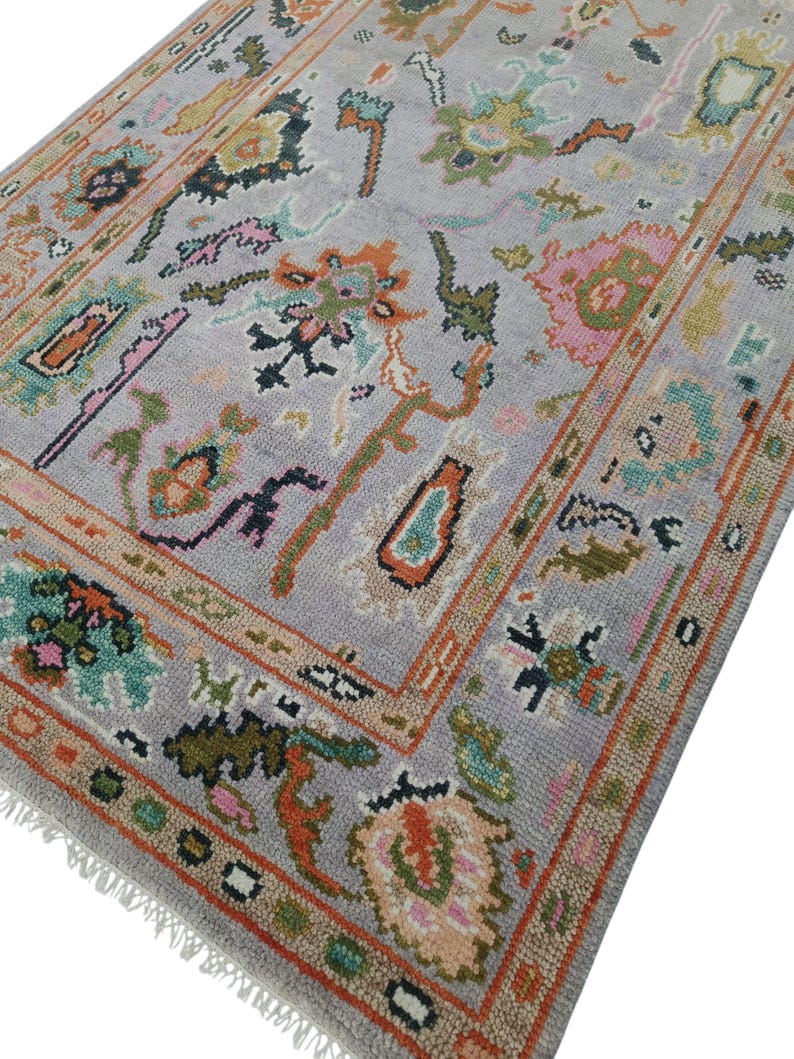 May include: A rectangular area rug with a light gray background and a colorful floral pattern. The rug features a border with orange, brown, and green accents. The design includes pink, orange, and green floral motifs.