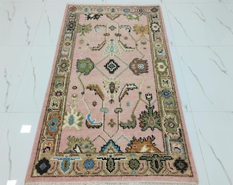 May include: A rectangular, hand-knotted rug with a pink field and a detailed border. The rug features a central floral design in shades of green, blue, brown, and cream. The border is a mix of floral and geometric patterns.