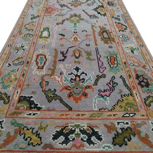 May include: A rectangular, hand-knotted rug with a light gray field and a detailed border. The rug features a complex floral pattern in shades of orange, pink, green, and black. The rug has a fringe on the short ends.