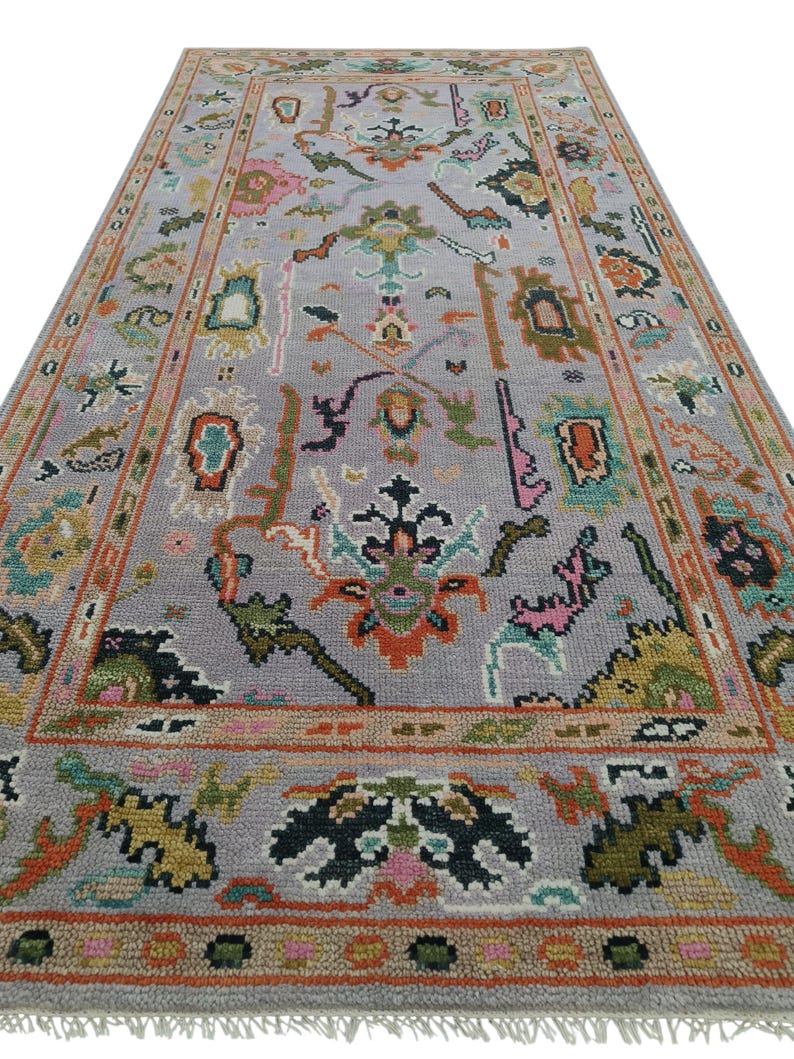 May include: A rectangular, hand-knotted rug with a light gray field and a detailed border. The rug features a complex floral pattern in shades of orange, pink, green, and black. The rug has a fringe on the short ends.