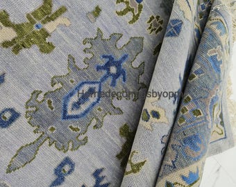 May include: A light blue rug with a detailed pattern in shades of blue, green, and beige. The rug has a textured appearance and a fringed edge. The design features floral and geometric shapes.