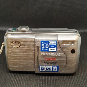 以下が含まれることがあります： シルバーのオリンパスC-50 ZOOMデジタルカメラ。5.0メガピクセルの解像度と充電式バッテリーを搭載。3倍光学ズームと12倍デジタルズームを搭載。ヘアライン仕上げの金属製です。