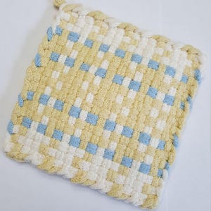 May include: A yellow and blue woven pot holder with a square shape and a braided edge.