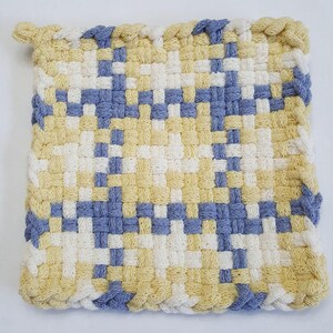 May include: A square, woven potholder with a repeating pattern of yellow, white, and blue squares. The edges are finished with a braided border in yellow and blue. This handmade item is designed for kitchen use.