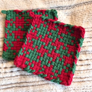 May include: Two woven potholders in a red and green checkerboard pattern. The potholders are square with a green border and a small loop for hanging. The weave is tight, creating a durable and heat-resistant surface.