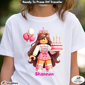 May include: A white t-shirt featuring a graphic of a block-style character with long brown hair wearing a pink birthday crown, a pink dress with the text "BIRTHDAY 8th", and holding a pink cake with three lit candles, accompanied by three balloons.