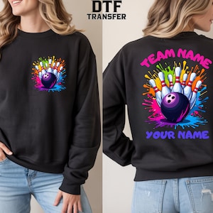 May include: A black crewneck sweatshirt featuring a bowling graphic with pins and a ball surrounded by a colorful paint splatter design. The front has a small chest print, while the back displays the same graphic with the text TEAM NAME and YOUR NAME.