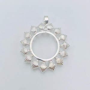 Può includere: Un ciondolo circolare in argento caratterizzato da un anello centrale aperto circondato da un bordo decorativo di piccoli motivi radianti a forma di conchiglia. L'oggetto include una piccola contromaglia sulla parte superiore e finitura lucida.