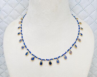 May include: An elegant necklace with gold-coloured teardrop pendants, each set with a blue gemstone. The necklace is displayed on a white mannequin. The design is delicate and refined, perfect for adding a touch of sophistication. The necklace is a beautiful piece of jewelry.