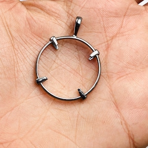 May include: A dark metallic circular pendant setting featuring four prongs extending inward from the rim to secure a gemstone. The pendant includes a small integrated bail at the top for attachment to a chain, showcasing a smooth, polished finish.