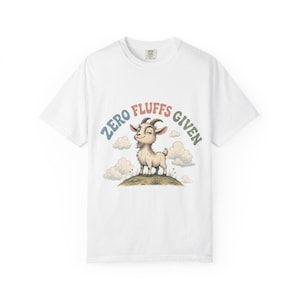 May include: White t-shirt featuring a cartoon goat on a hill with clouds. The text "ZERO FLUFFS GIVEN" is above the goat in blue, red, and green. The shirt has a crew neck and short sleeves. The design is printed on the front.
