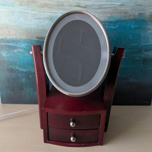 Vintage mahogany-colored wooden dressing table with 2 drawers, swiveling mirror and lighting.