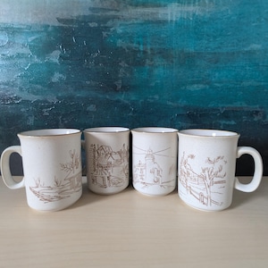 May include: A set of four off-white ceramic mugs, each featuring a unique brown line-art illustration. The designs include a rural landscape, a coastal building, a lighthouse, and a tree-lined fence, all with a speckled finish and brown rims.