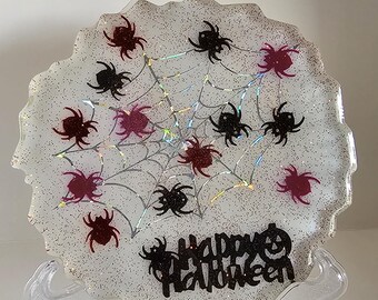 Peut inclure: Un dessous de verre décoratif sur le thème d'Halloween avec un fond blanc scintillant. Le dessous de verre présente un motif de toile d'araignée avec des araignées noires et bordeaux. Les mots "Happy Halloween" sont écrits en noir.