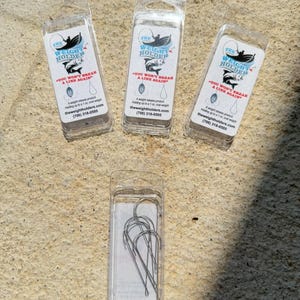 May include: Three clear plastic packages of fishing accessories. Each package has a white label with the text "THE WEIGHT HOLDER" and "YOU WON'T BREAK A LINE AGAIN". The bottom package contains several fishing hooks.