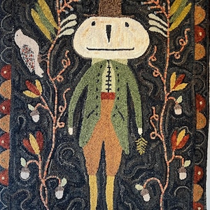 May include: A whimsical, hand-hooked rug featuring a figure with a large, oval head, wearing a green jacket, orange pants, and a brown top hat. The rug has a dark background with floral and bird accents, and measures approximately 36 inches by 48 inches.