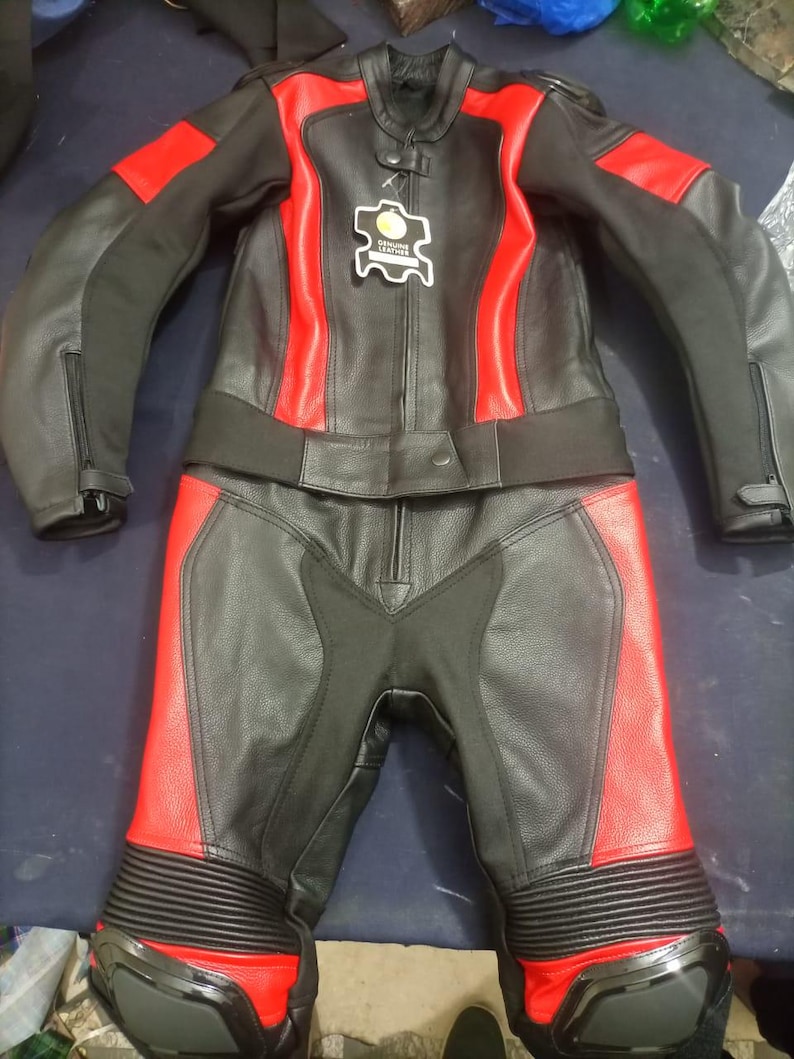 May include: Black and red leather motorcycle suit. The suit includes a jacket and pants. The jacket has red accents on the shoulders and sides. The pants have red accents on the lower legs. The suit has a tag that says "Genuine Leather".
