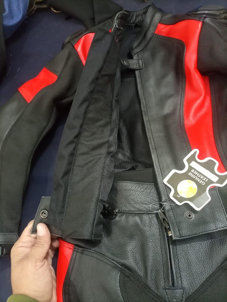 May include: Black and red leather motorcycle jacket and pants set. The jacket has red accents on the shoulders and sleeves. The pants have red accents on the sides. A tag that says "GENUINE LEATHER" is attached to the jacket.