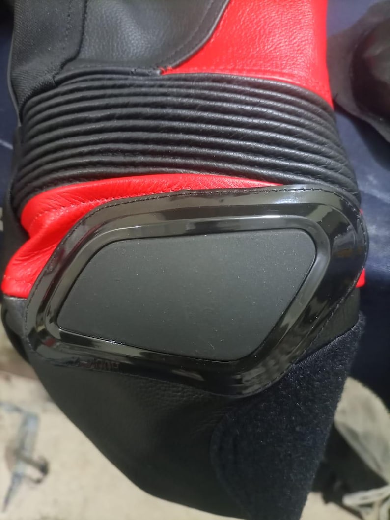 May include: Close-up of a black and red motorcycle boot. The boot features a black protective panel, ribbed detailing, and a red leather upper. The design suggests a focus on protection and performance.