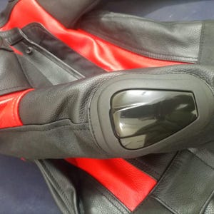 May include: Black and red motorcycle jacket with protective elbow pads. The jacket features black leather panels with red accents on the shoulders and torso. The elbow pads are glossy black.