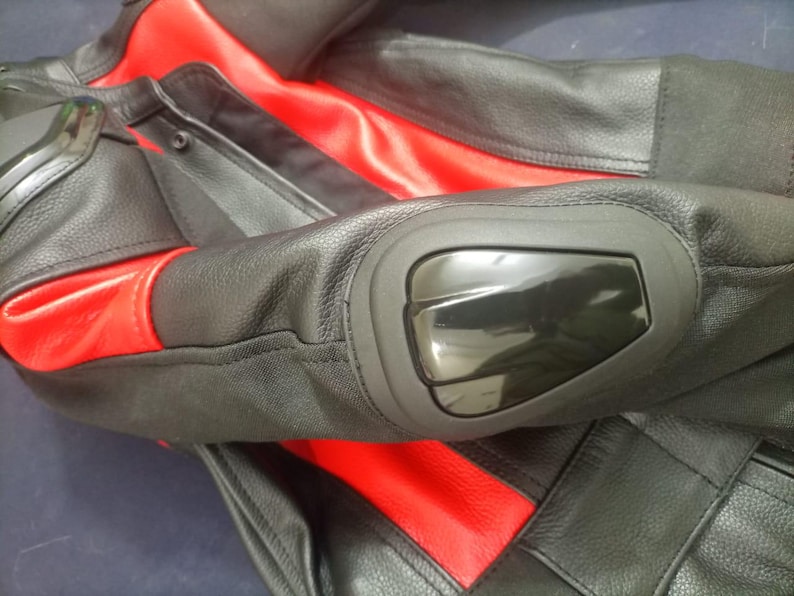 May include: Black and red motorcycle jacket with protective elbow pads. The jacket features black leather panels with red accents on the shoulders and torso. The elbow pads are glossy black.