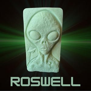 Puede incluir: Una escultura rectangular verde claro de un rostro alienígena con grandes ojos ovalados y una boca pequeña. La palabra "ROSWELL" está impresa en negrita, con una fuente sans-serif en la parte inferior de la imagen. El fondo tiene un degradado verde y negro.