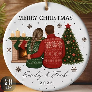 May include: A white ceramic Christmas ornament. It features the text "Merry Christmas", the names "Emily & Jack", and the year "2025". The ornament depicts a couple, a Christmas tree, and a fireplace.