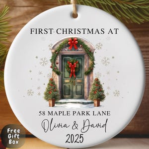 May include: A white ceramic Christmas ornament featuring the text "FIRST CHRISTMAS AT" and a watercolour illustration of a green door adorned with a wreath and red bow. The ornament also includes the address "58 MAPLE PARK LANE", the names "Olivia & David", and the year "2025".