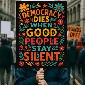 K&ouml;nnte beinhalten: Ein schwarzes Schild mit den Worten "DEMOCRACY DIES WHEN GOOD PEOPLE STAY SILENT" in bunten Buchstaben. Das Schild wird in einer Menschenmenge hochgehalten. Florale und Blattmotive umgeben den Text.