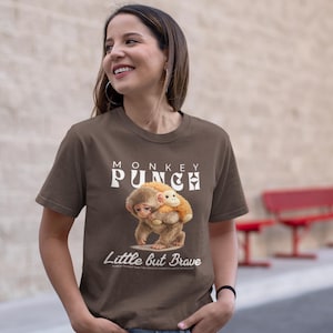 Peut inclure: T-shirt marron avec une illustration de dessin animé de deux singes. Le texte "MONKEY PUNCH" est au-dessus de l'illustration, avec "Little but Brave" en dessous. Le t-shirt est porté par une personne.