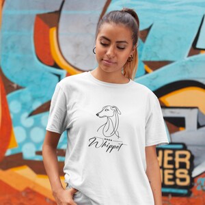 Può includere: T-shirt bianca con un disegno a tratto minimalista nero di un cane Whippet e la parola "Whippet" in corsivo. La maglietta è realizzata in un materiale morbido. Il design è un'illustrazione semplice ed elegante.