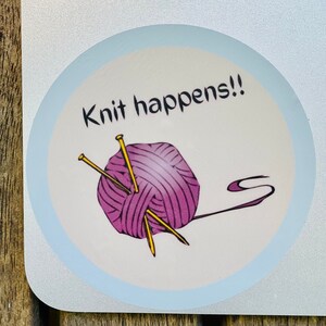 May include: A white sticker with a blue border on a silver laptop. The sticker has a pink ball of yarn with two yellow knitting needles and the text "Knit happens!!"