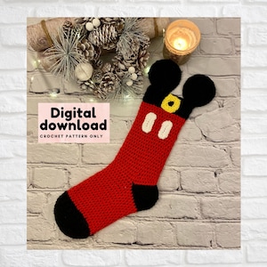 May include: Red and black crocheted stocking with Mickey Mouse ears, eyes, and nose. The stocking is on a white brick background. Digital download crochet pattern only.