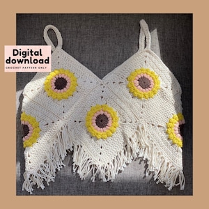 Könnte beinhalten: Häkeltop mit Sonnenblumenmuster. Das Oberteil ist weiß mit gelben und braunen Akzenten. Das Oberteil hat einen Fransenbesatz.