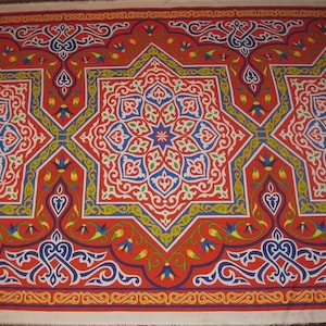 May include: A vibrant textile featuring a repeating geometric pattern in red, blue, yellow, and white. The design includes star-like shapes and floral motifs, creating a rich, ornate appearance. The overall style suggests a cultural or ethnic influence.