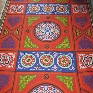 May include: A rectangular fabric with a repeating pattern of geometric shapes and floral designs. The fabric features a red background with blue, white, green, and yellow accents. The design includes circular and square motifs.