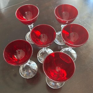 May include: Set of six vintage red wine glasses. Each glass features a clear stem and a vibrant red bowl. The glasses are arranged in a circular pattern, showcasing their elegant design and color.