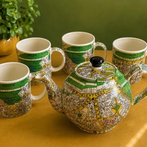 May include: A ceramic teapot and four matching mugs featuring a detailed map print of London, including street names like Knightsbridge and Green Park. The set has a white interior, a rounded teapot body with a black lid knob, and a colorful map design.