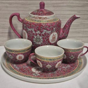 May include: A vintage tea set comprising a teapot with lid, three teacups, and a serving tray. The set is predominantly burgundy with white and gold detailing, and includes Chinese characters. The teapot and cups have handles.