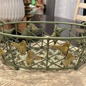Peut inclure: Panier ovale en métal avec une finition vert vieilli et des accents de feuilles dorées. Le panier a deux poignées arquées et un motif en treillis. Rangement décoratif pour la décoration intérieure.