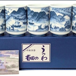 May include: A set of five blue and white ceramic tea cups, each with a different landscape scene. The cups, presented in a blue box, depict mountains, trees, and figures. The box includes Japanese text and a small picture.