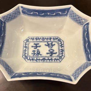 May include: White ceramic dish with an octagonal shape and blue decorative trim. The dish features a central rectangular design with Chinese characters. A classic piece for serving or display.