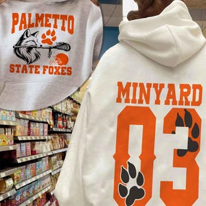 May include: A white hooded sweatshirt featuring the orange text MINYARD and the number 03 with black paw prints on the back. The inset shows a grey hooded sweatshirt with the orange text PALMETTO STATE FOXES, a fox illustration, and a lacrosse stick.