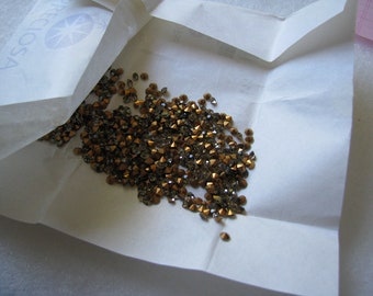 May include: A white paper bag with a pile of small, gold-colored rhinestones inside.
