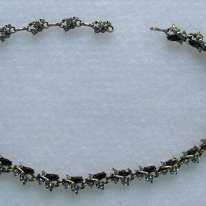 May include: A delicate gold chain necklace with blue and clear rhinestones arranged in a floral pattern.