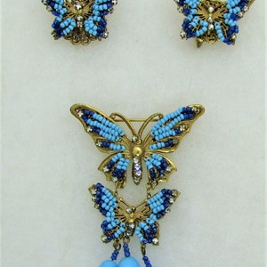 May include: A set of three blue and gold butterfly brooches. The largest brooch has two smaller butterflies dangling from it, and all three have blue and clear bead accents.