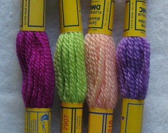 May include: Four skeins of embroidery floss in different colors: purple, green, pink, and lavender. Each skein has a yellow label with the DMC brand name, the color number, and the text "Laine Divisibl Floral" and "Pullskein".
